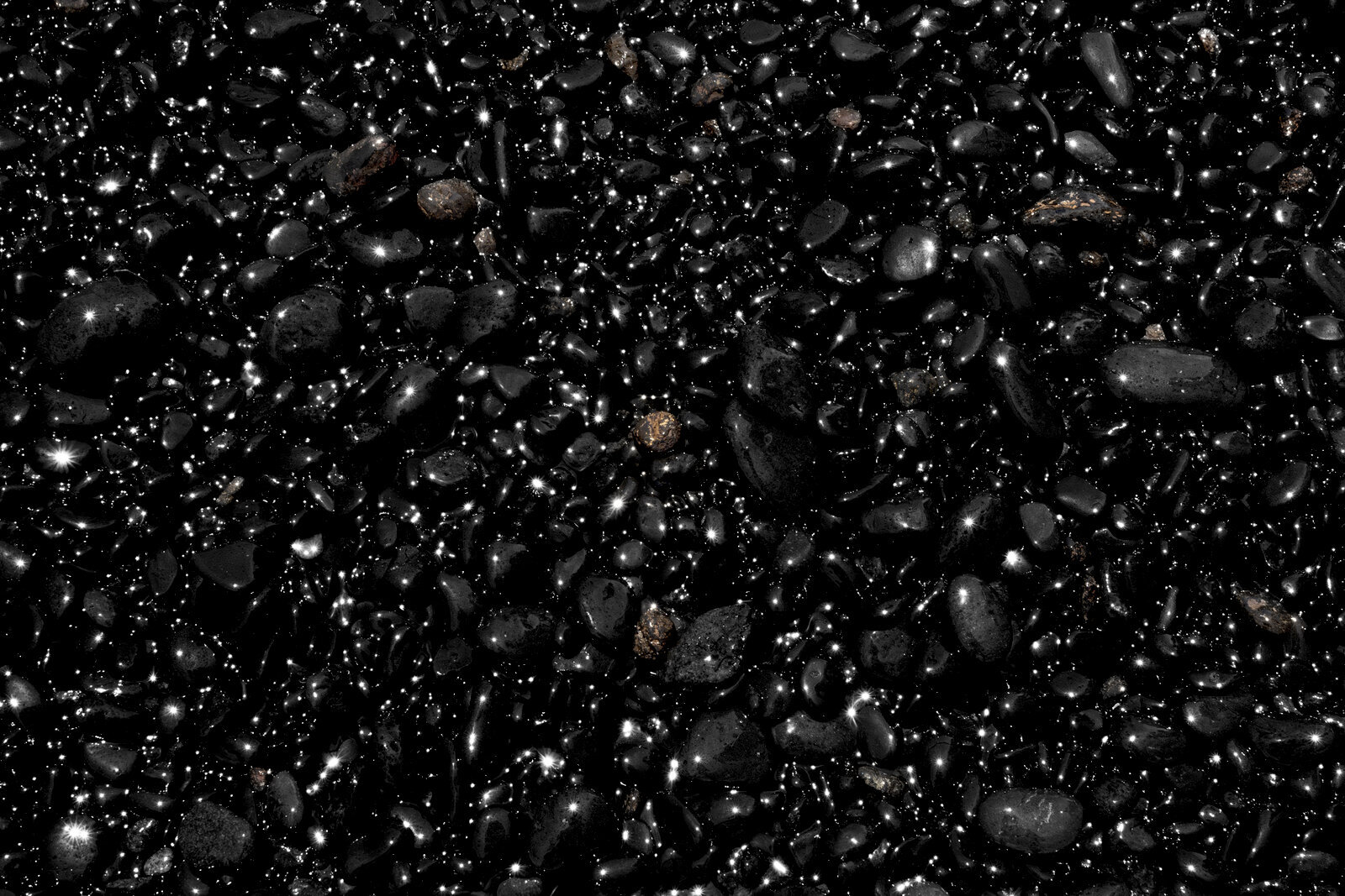 Black, smooth rocks polished by the relentless tide of the ocean. Sun stars can be seen in the reflection of the wet rocks.