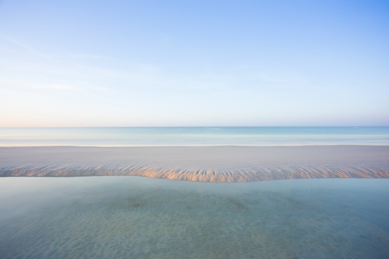Peaceful blue tones over a calm shoreline at dawn