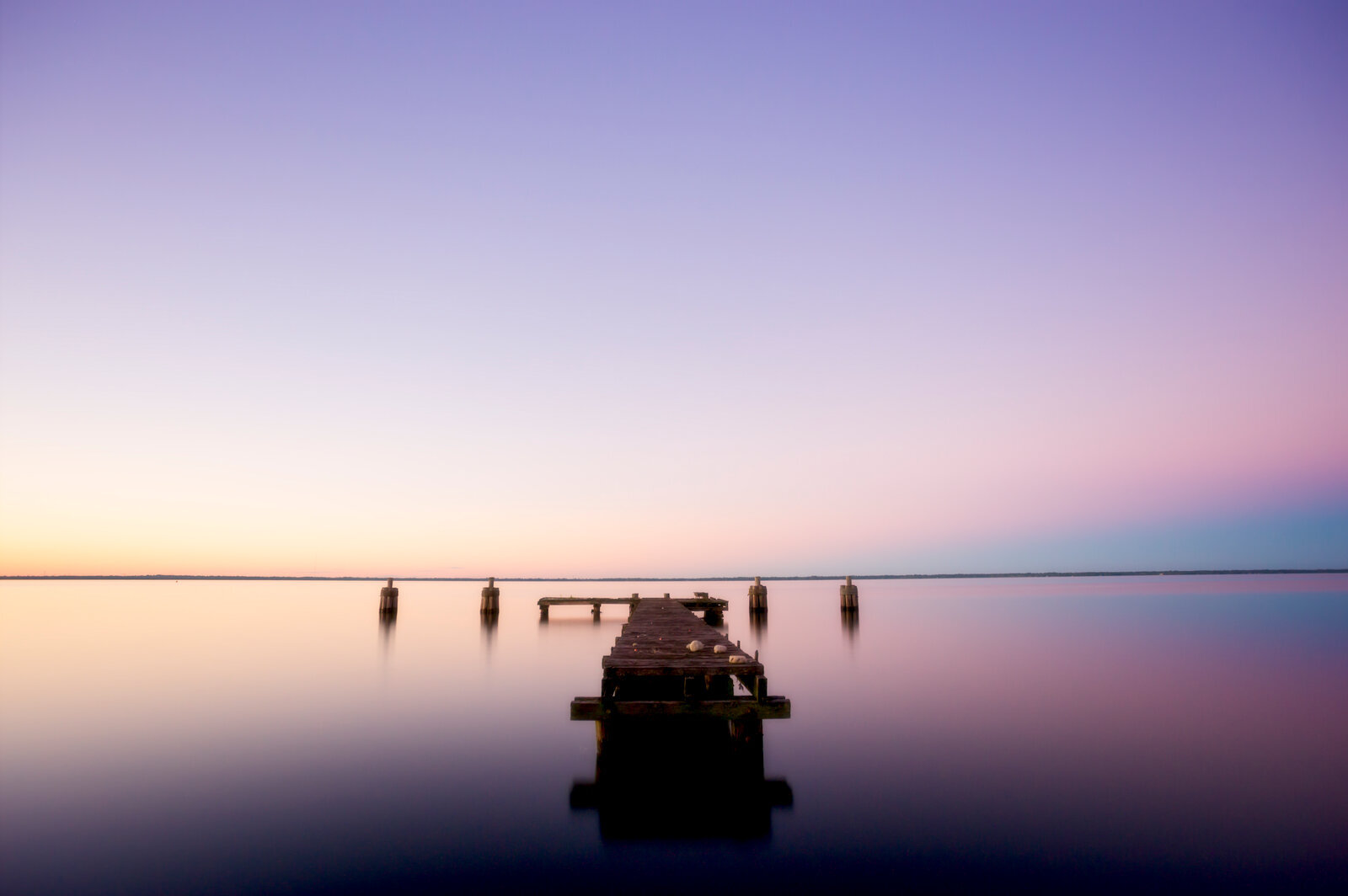 Wooden dock fades into calm water under twilight glow