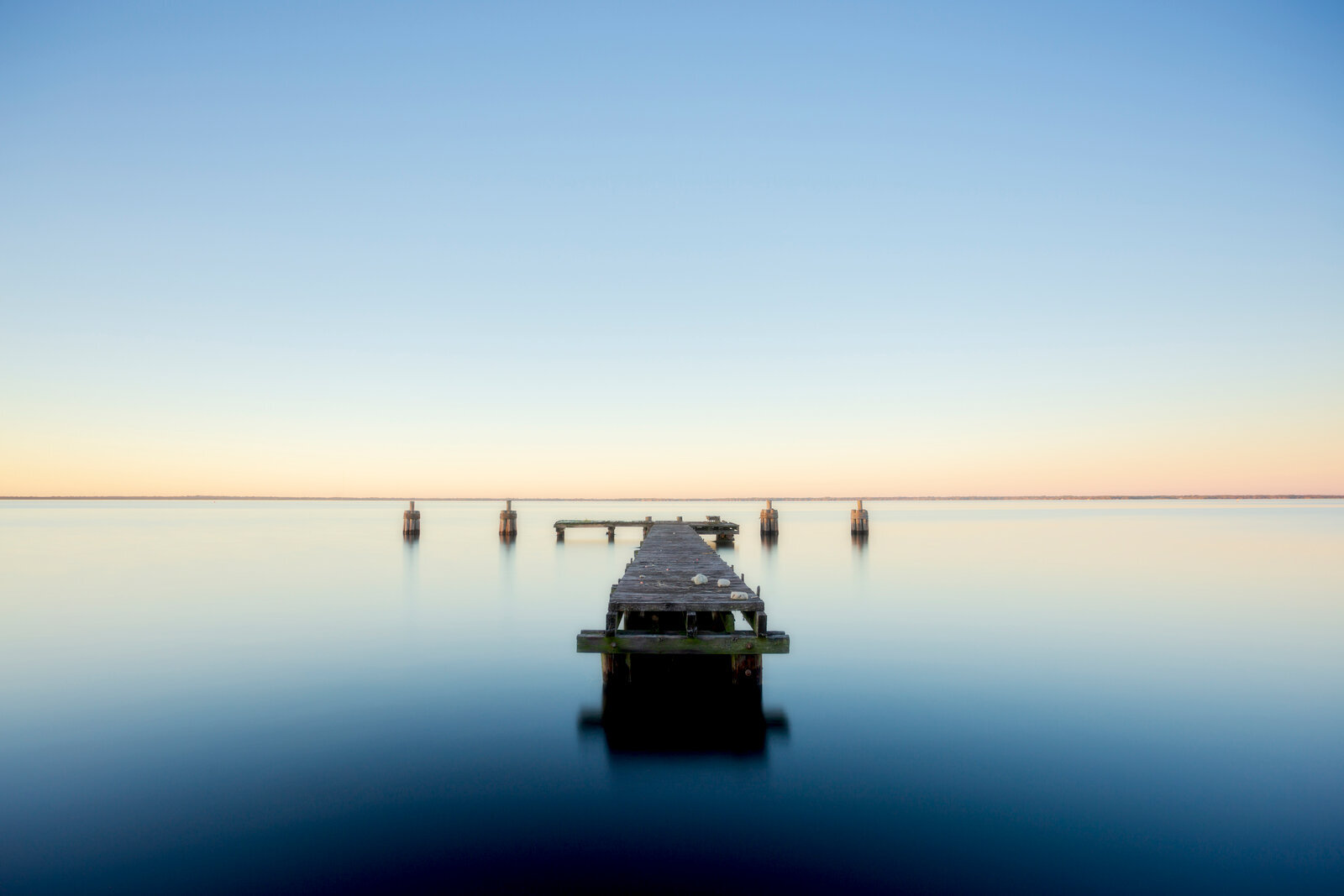 Old dock posts submerged in floodwater at sunrise with glowing reflections